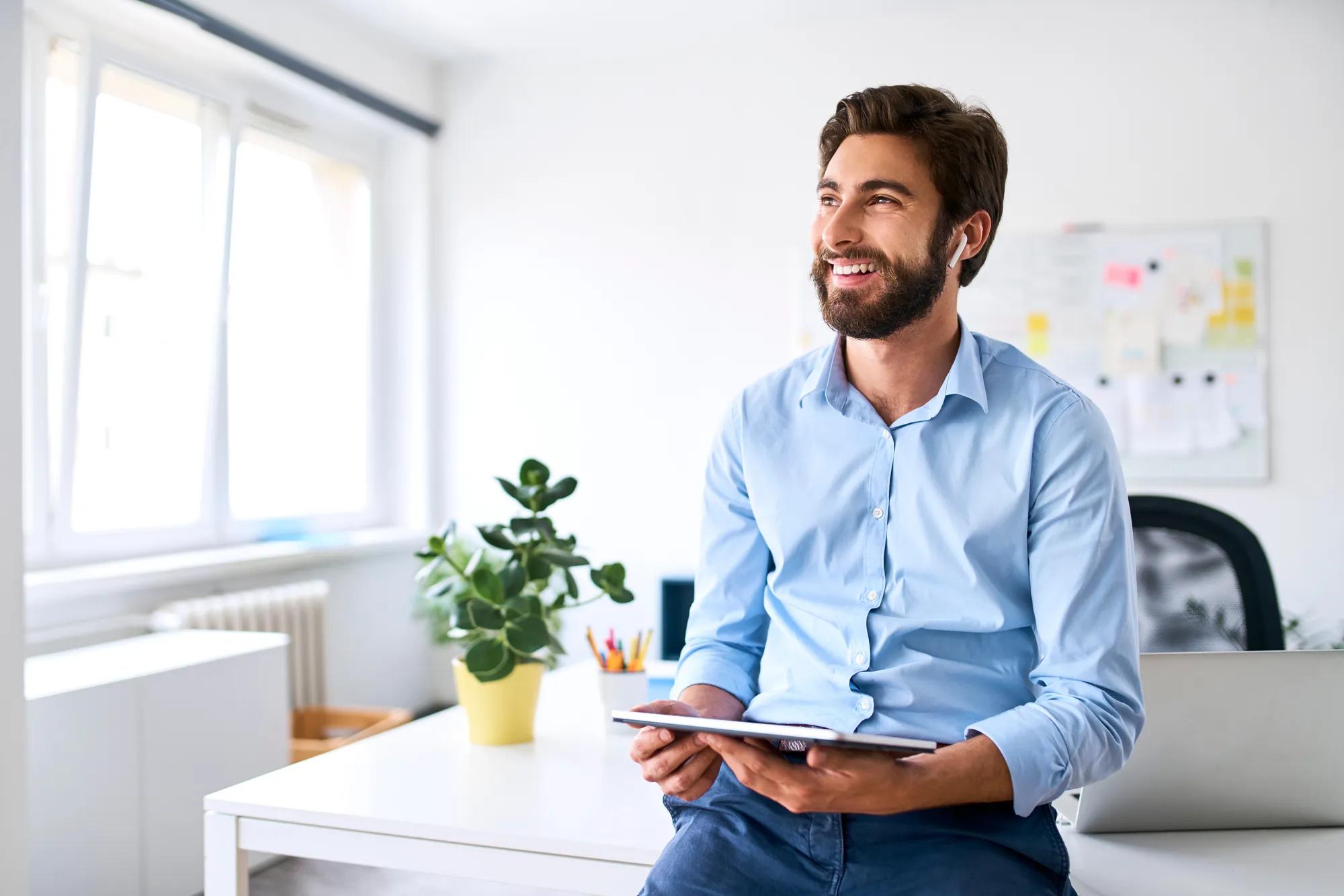 Smiling businessman with headphones using a digital tablet in his office