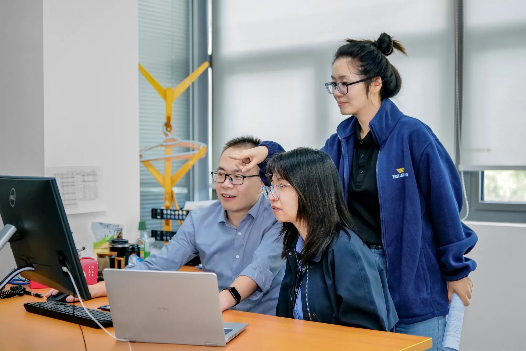 Three employees at the Trelleborg Wuxi Boots facility collaborate to analyze key automotive market data displayed on a computer screen.