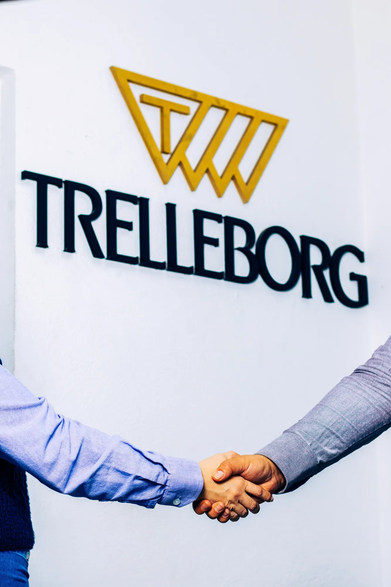 A handshake between two employees in front of the Trelleborg logo, representing partnership and teamwork.
