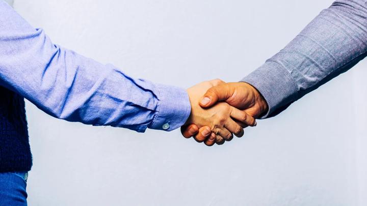 A handshake between two employees in front of the Trelleborg logo, representing partnership and teamwork.