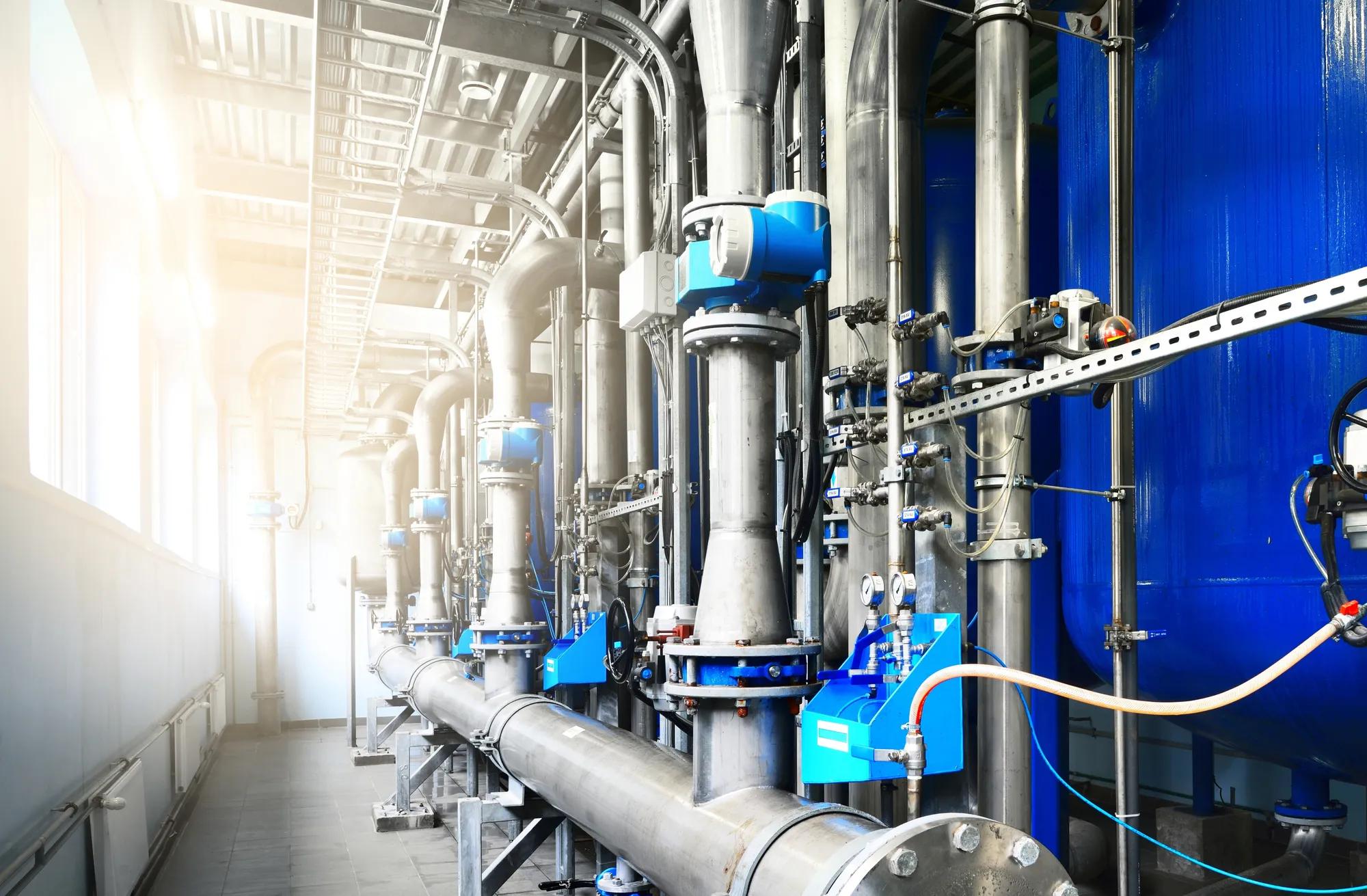 Large industrial water treatment and boiler room. Shiny steel metal pipes and blue pumps and valves. Adobe Stock 396197014