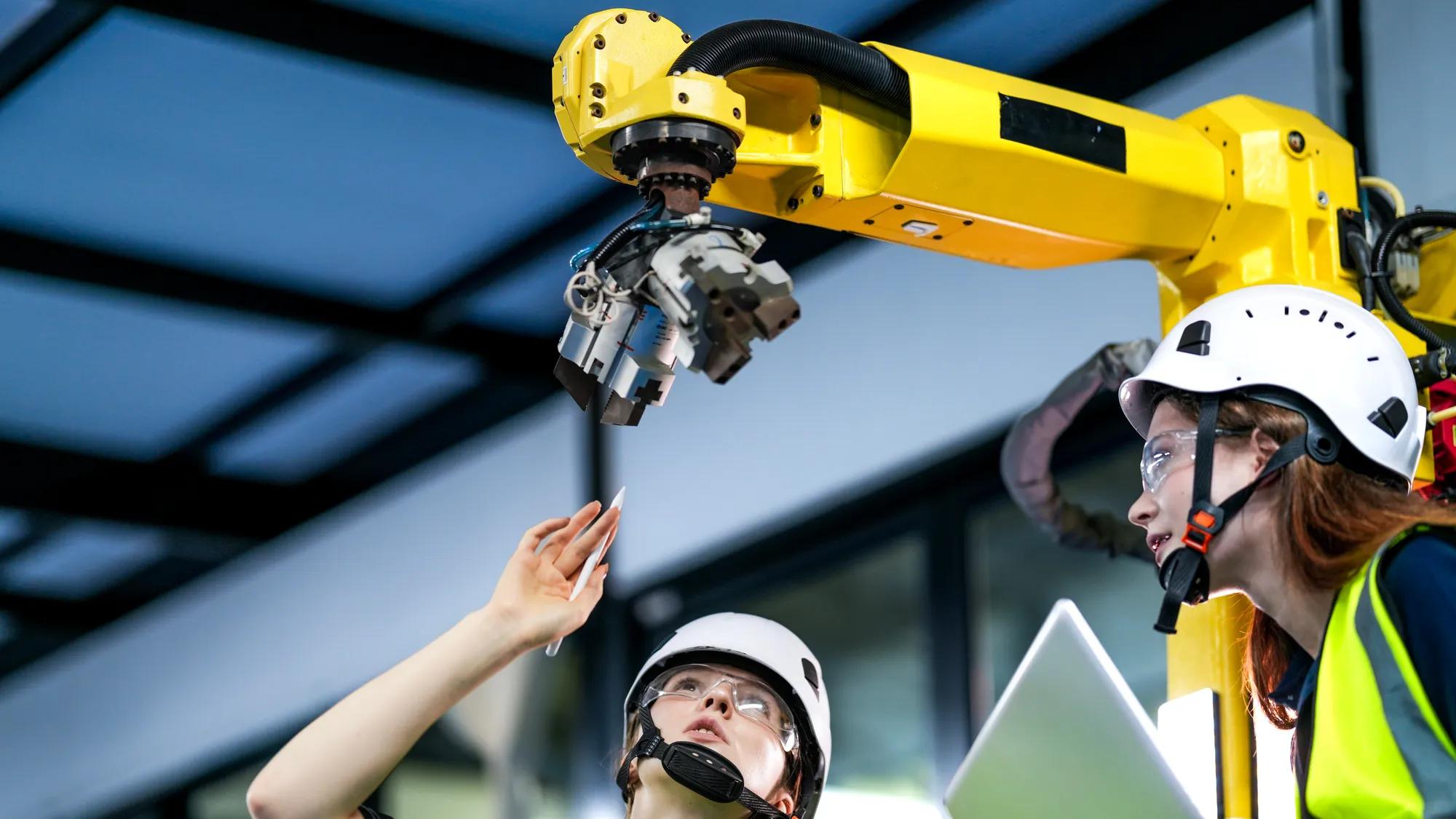 Two female robotics engineers in an R and D lab program an artificial intelligence system. They are testing the hardware and motion control of a large industrial robot.