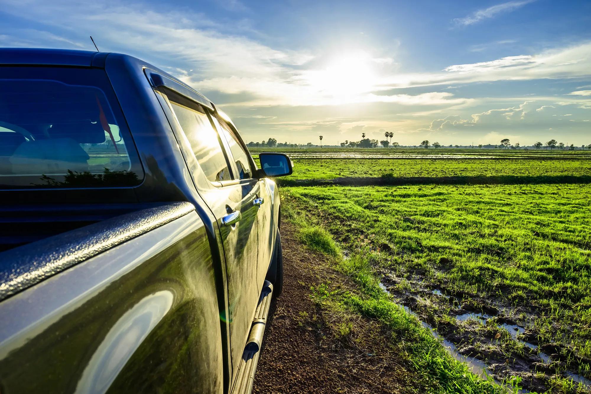Part of pickup truck on the dirt road at the rice field before sunset, travel along the countryside