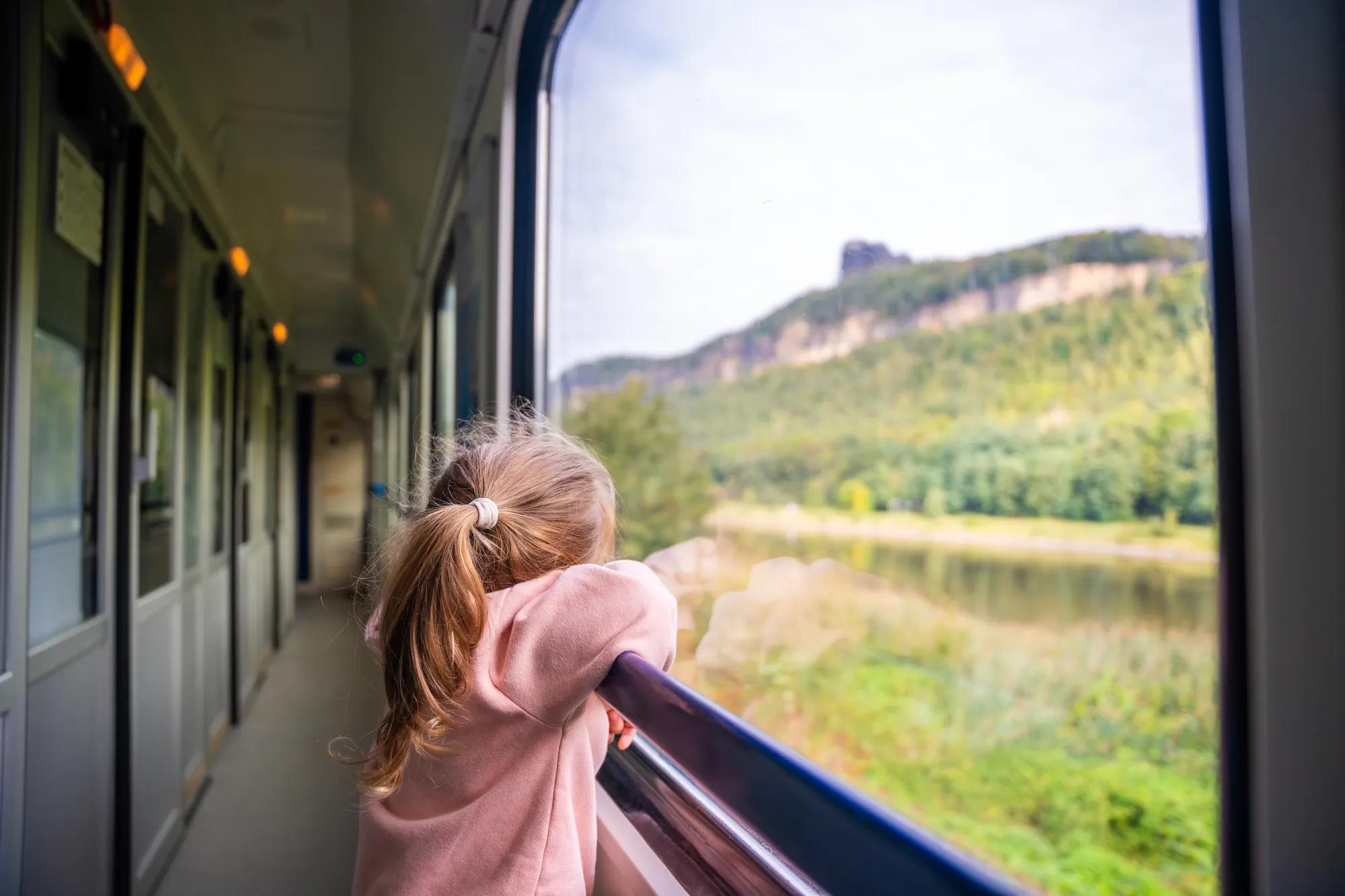 Little girl looking out train window outside, while it moving. Traveling by railway, Europe. High quality photo