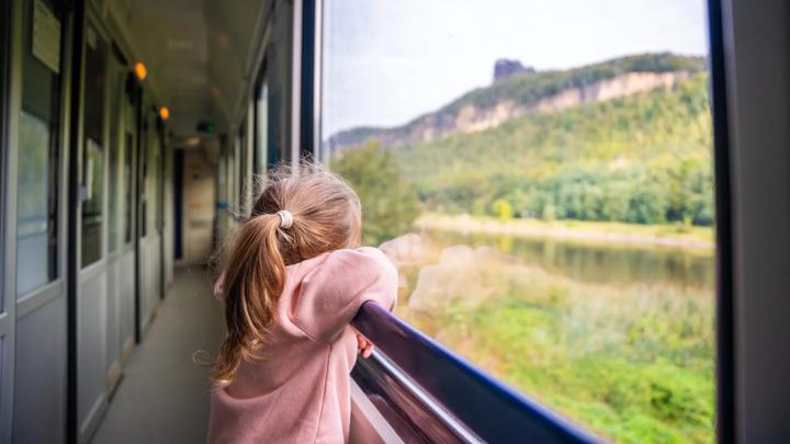 Little girl looking out train window outside, while it moving. Traveling by railway, Europe. High quality photo