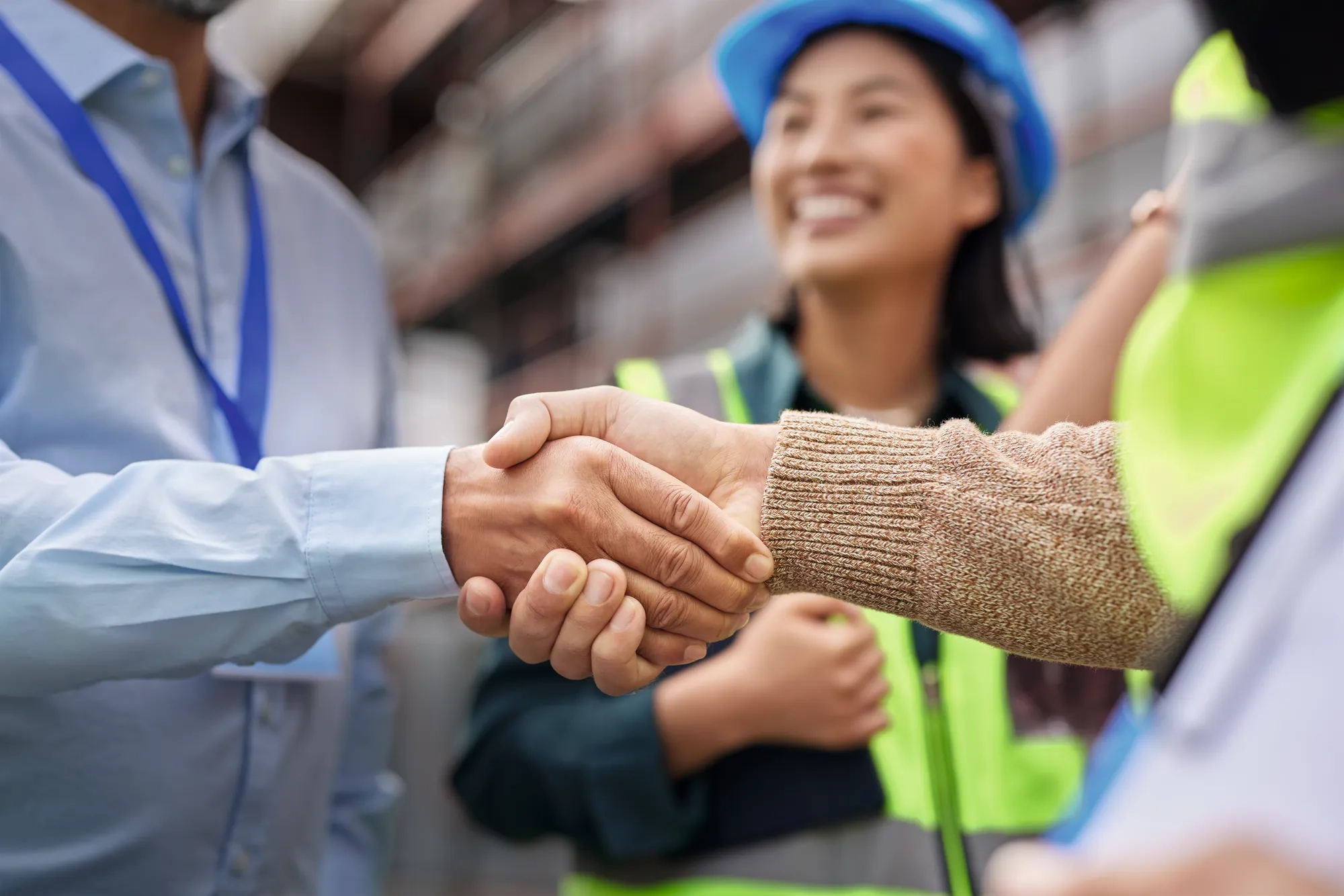 Close up of a handshake between construction worker and foreman sealing a deal on site. Businessman and architect shaking hands as a symbol of partnership at construction site. Agreement reached as colleagues shake hands at a building site with a worker in the background.