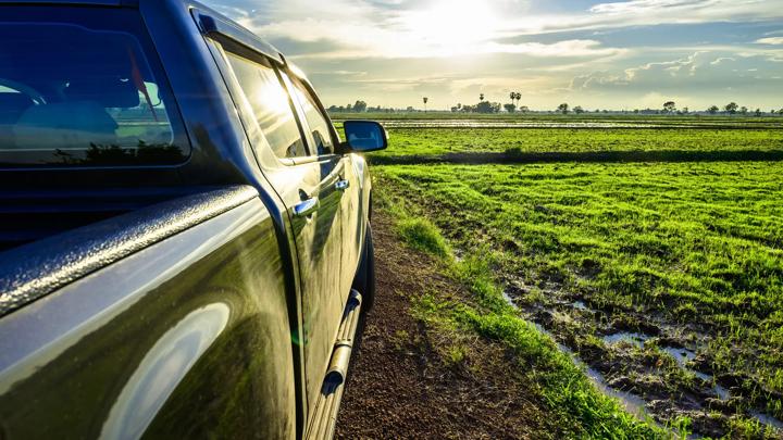 Part of pickup truck on the dirt road at the rice field before sunset, travel along the countryside