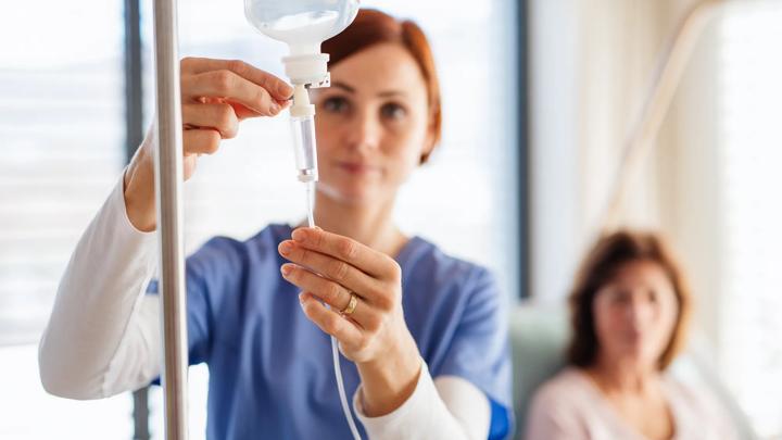 A front view of nurse with IV drip and patient in bed in hospital room.