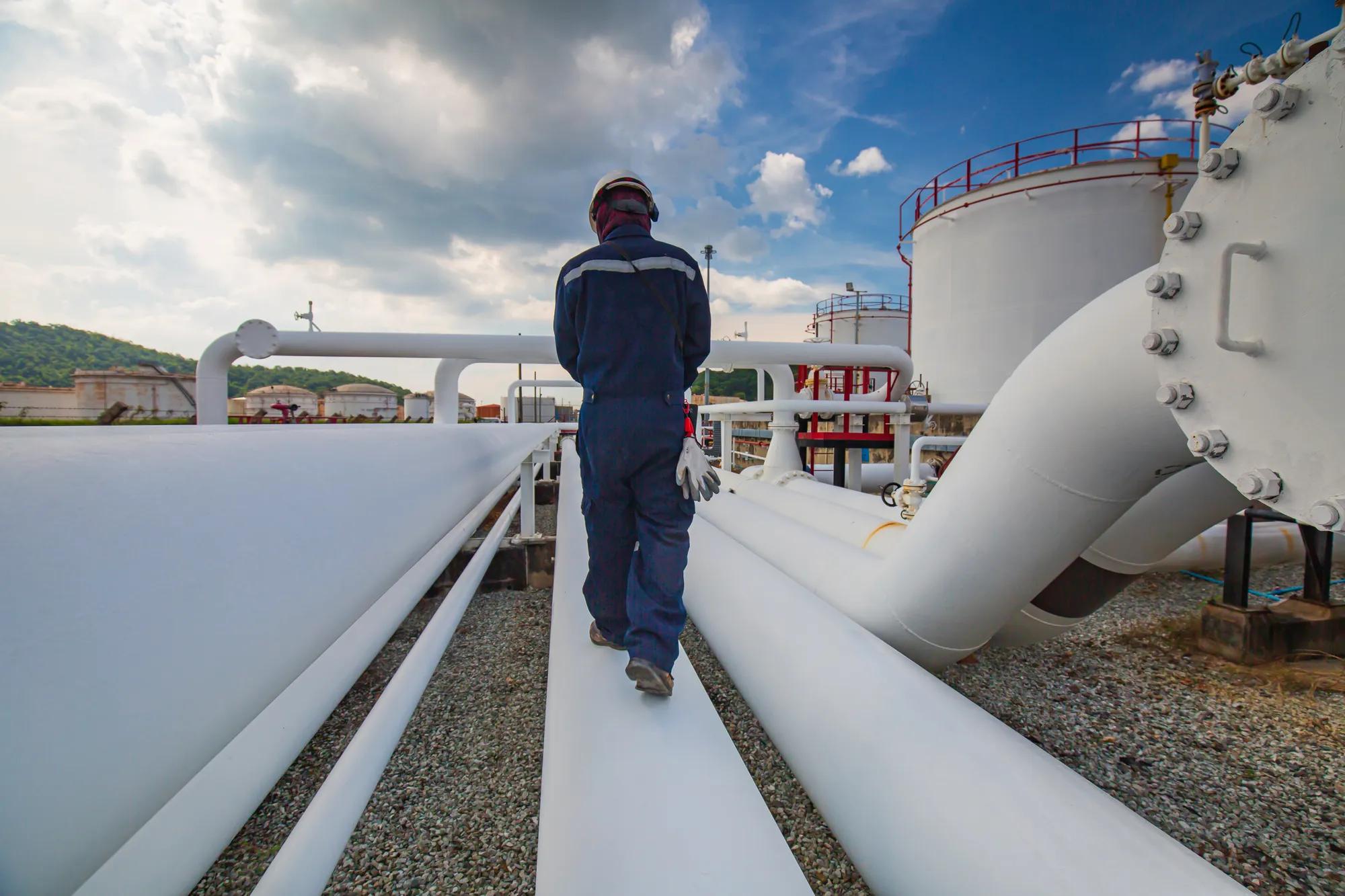 Male worker inspection at steel long pipes and pipe elbow in station oil factory during refinery valve of visual check record pipeline oil and gas industry.