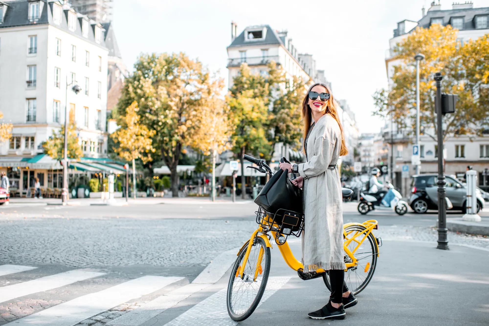 Portrait of a young stylish woman with yellow bicycle on the street in Paris
