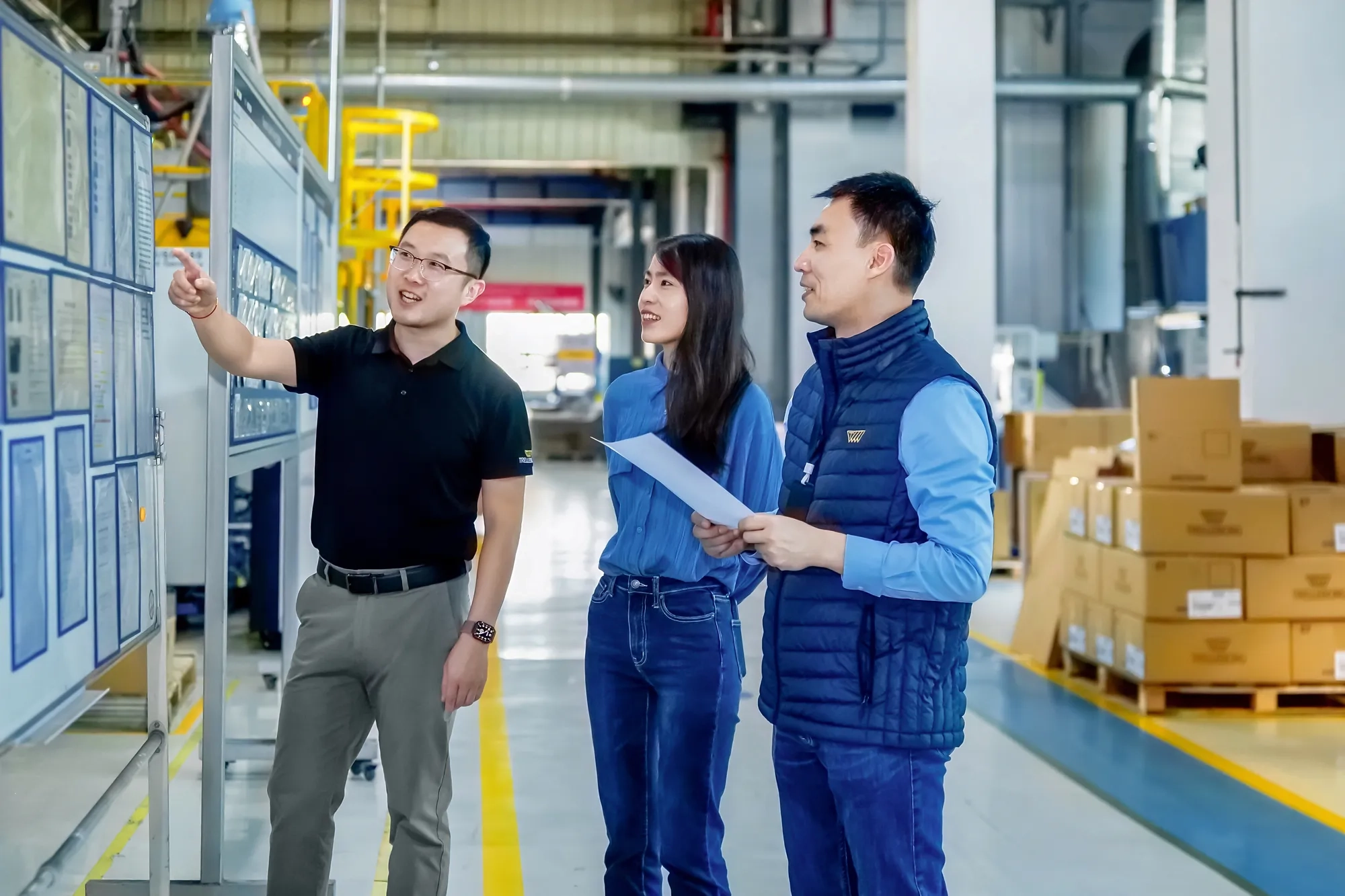 The operations director and two managers analyze and discuss information displayed on the production board.