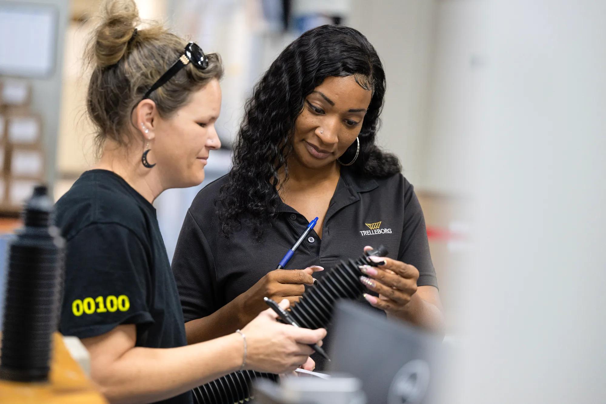 As part of visual quality control, two operators inspect newly produced rack and pinion boots on a rack, ensuring consistent quality and compliance with automotive industry standards.