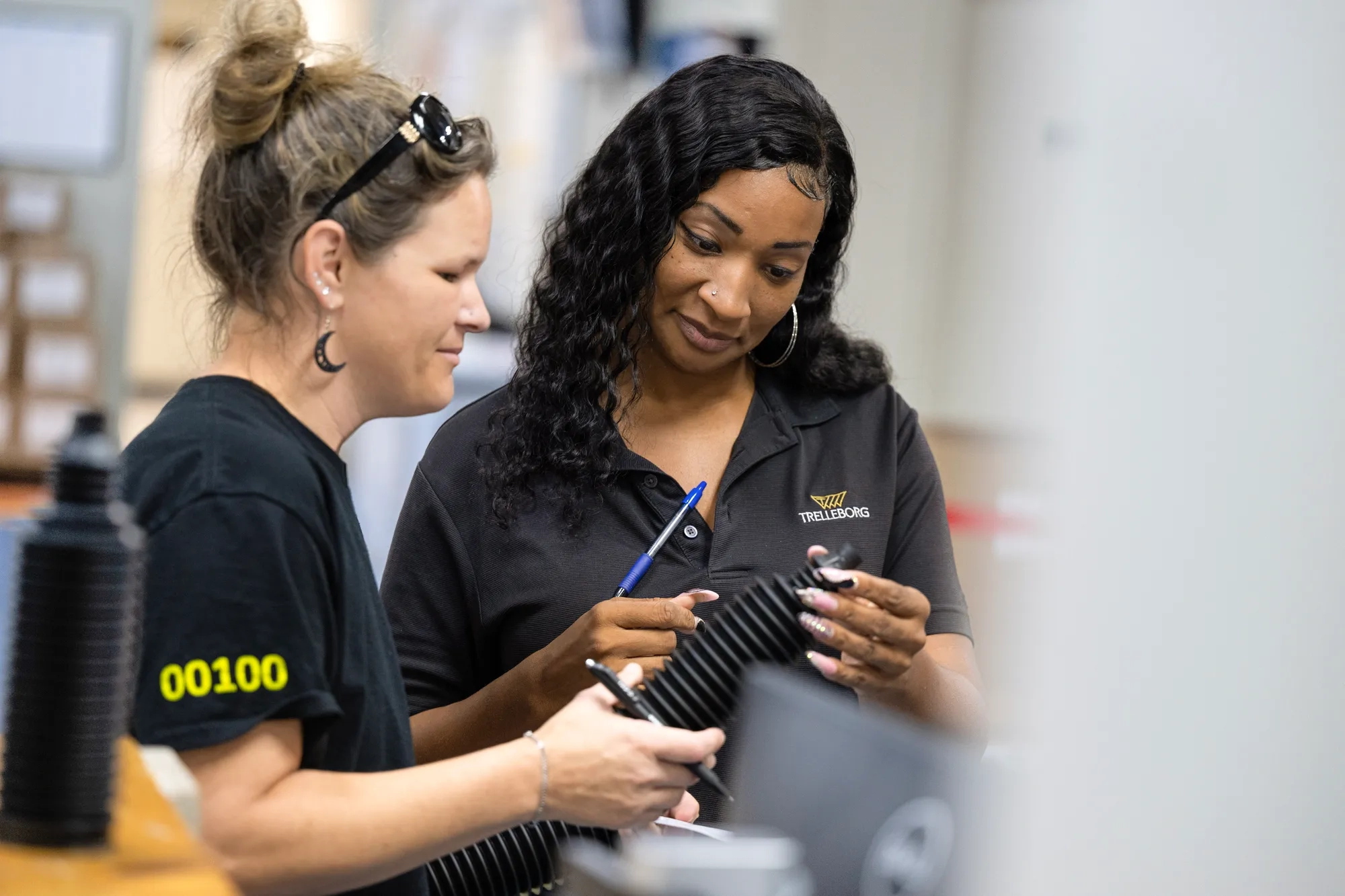 As part of visual quality control, two operators inspect newly produced rack and pinion boots on a rack, ensuring consistent quality and compliance with automotive industry standards.