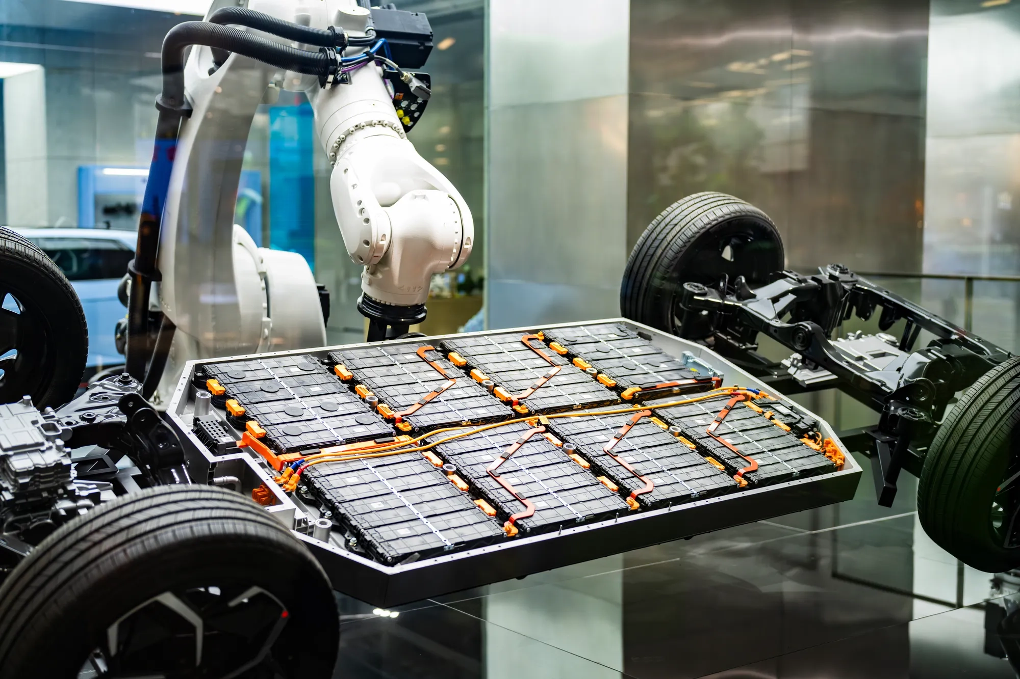 An industrial robotic arm installs a battery pack on an electric car chassis, showcasing advanced technology in automotive manufacturing and sustainable transportation solutions.
